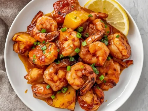 A serving of BBQ glazed shrimp with fresh pineapple slices on a plate.