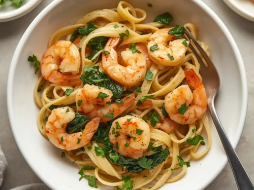 Close-up of garlic shrimp linguine with fresh spinach leaves and red pepper flakes in a bowl