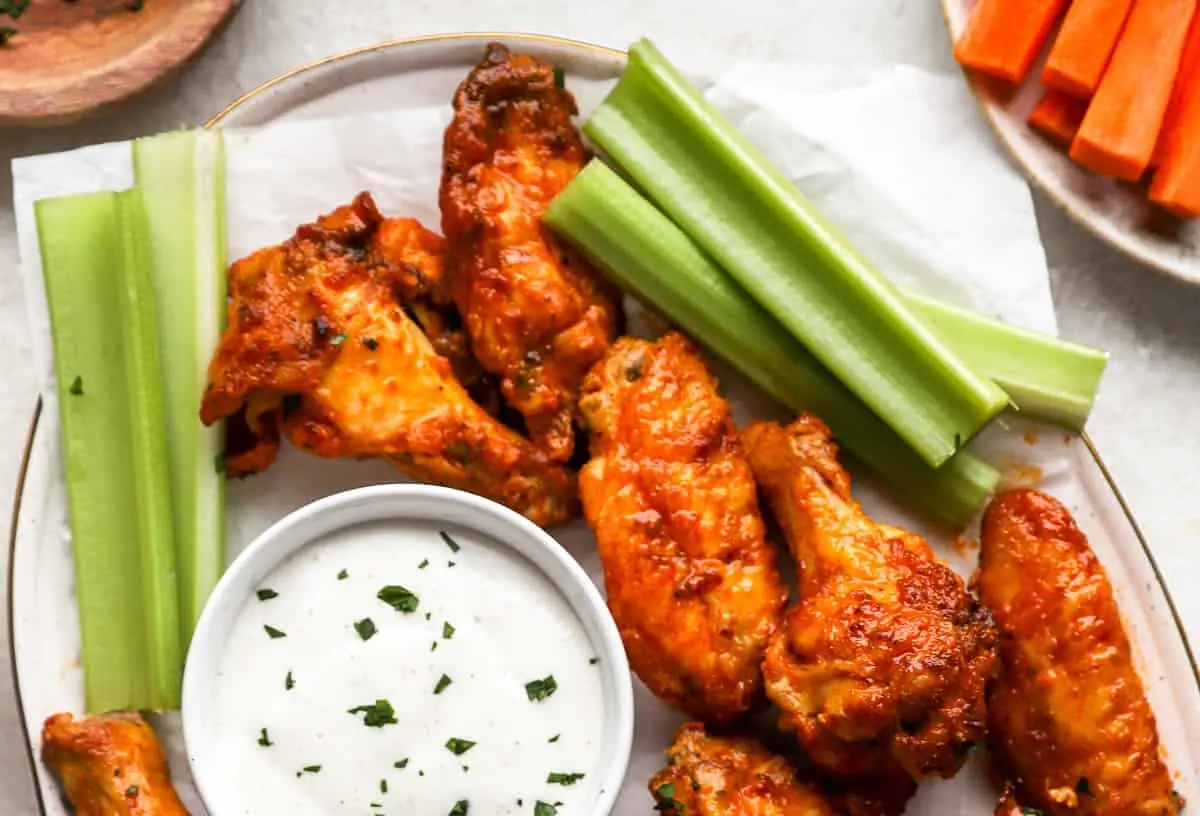 A plate piled high with crispy, saucy buffalo wings, ready to be eaten.